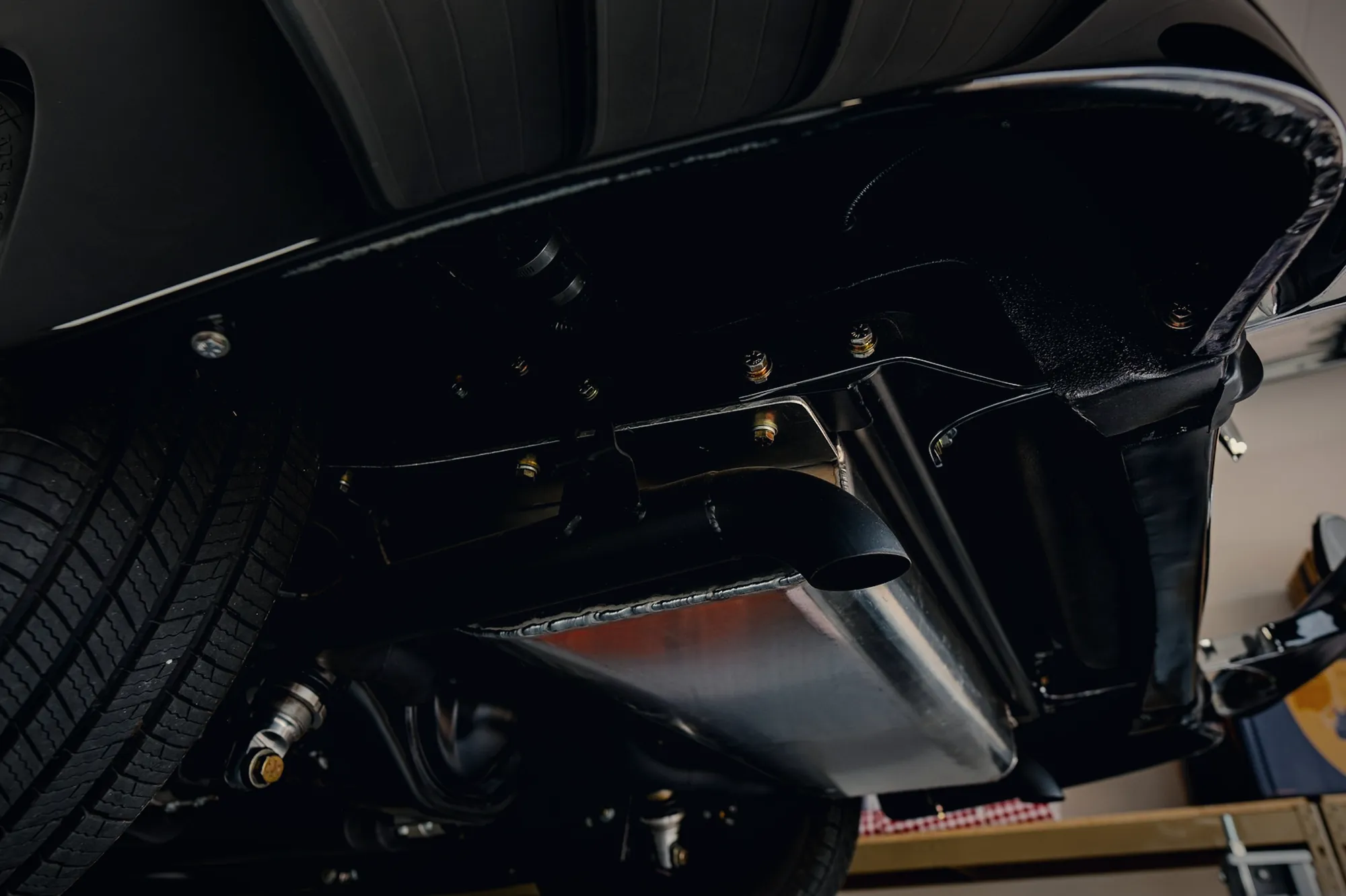 The underside of a car on a hoist, showing the exhaust, suspension and floor pan